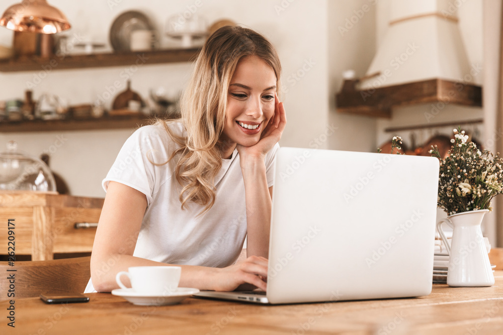 Portrait of satisfied blond woman working on laptop and drinking coffee while sitting in cozy cafe indoor Portrait of satisfied blond woman working on laptop and drinking coffee while sitting in cozy cafe indoor