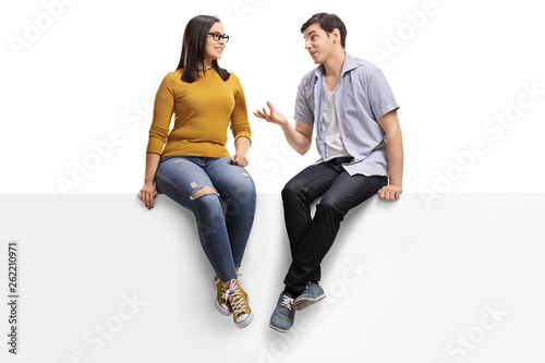 Young man sitting on a blank signboard and talking to a young woman photo