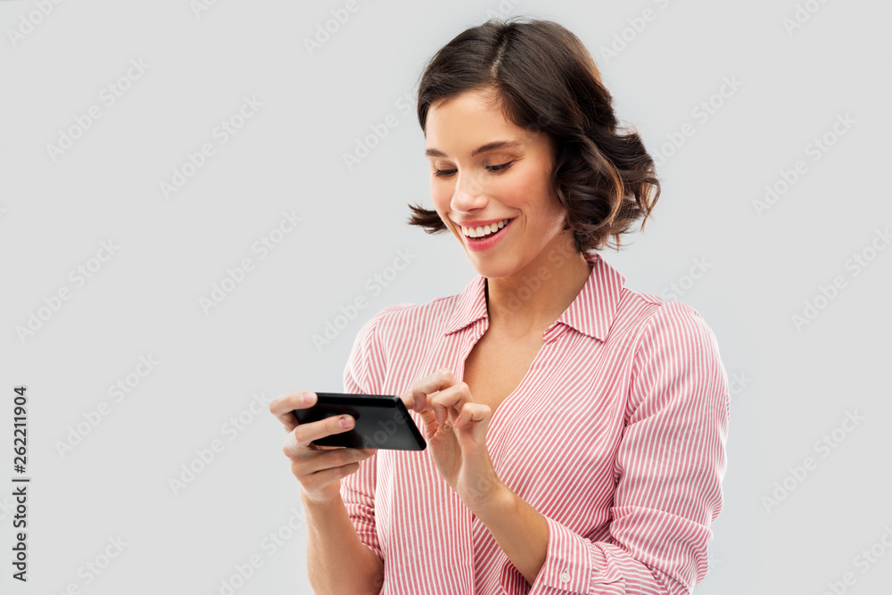 technology and people concept - happy smiling young woman in striped shirt using smartphone over grey background technology and people concept - happy smiling young woman in striped shirt using smartphone over grey background