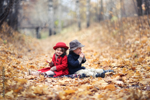 boy and girl are sitting on autumn leaves and eat