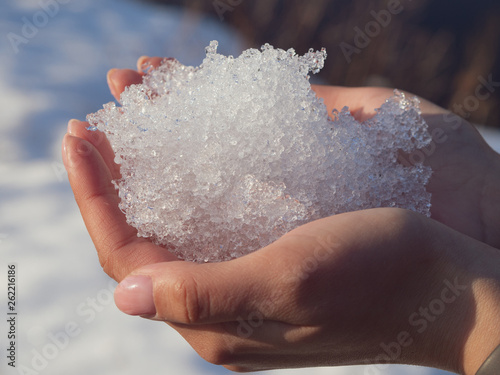 A young women hands holding melting snow sparkling in the sun; transparent cristals of water in the hands; sunny spring weather, cristal clear ice; new season in nature
