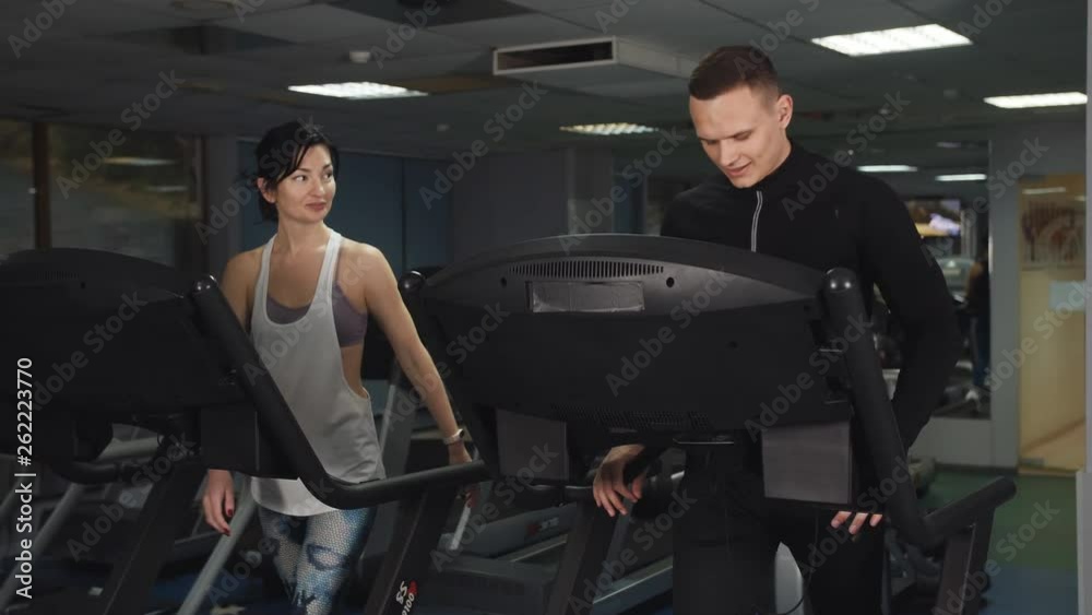 Man and woman train together on the treadmill at the athletic club.