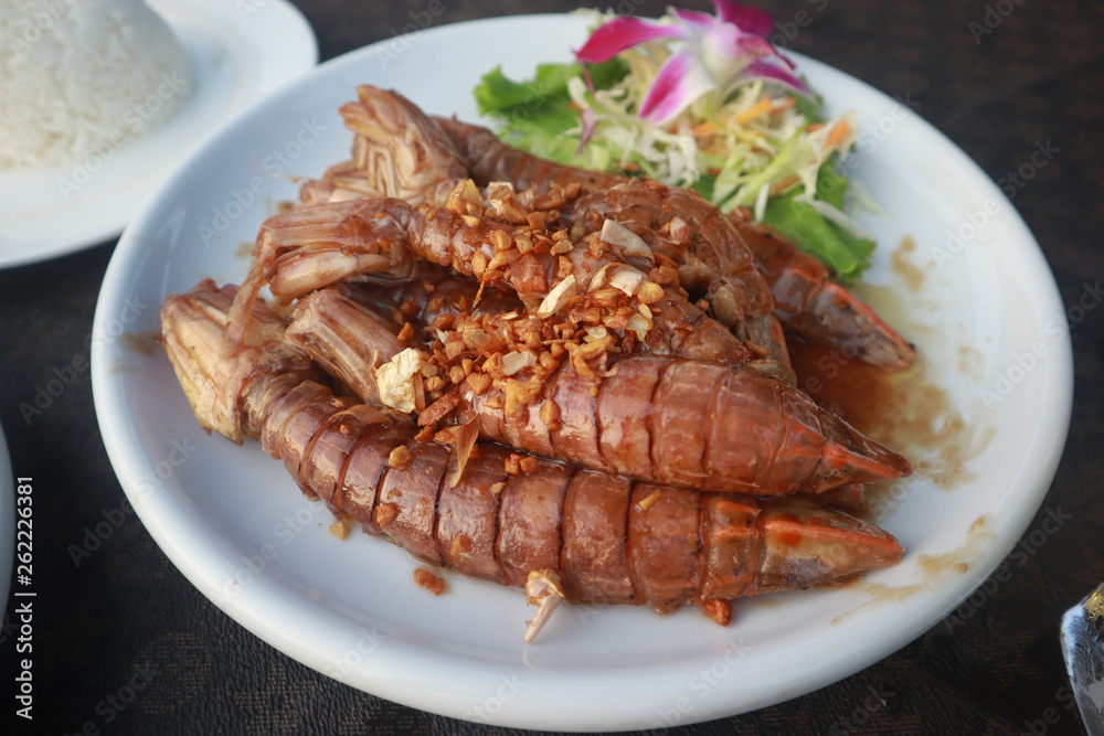 Fried crayfish with garlic decorated with purple orchid on a white ceramic dish put on leather floor the grid pattern. Fried crayfish with garlic decorated with purple orchid on a white ceramic dish put on leather floor the grid pattern.
