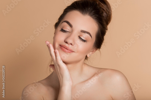 Beautiful face portrait of young woman is applying face cream on a cheek. Skin care and health concept.