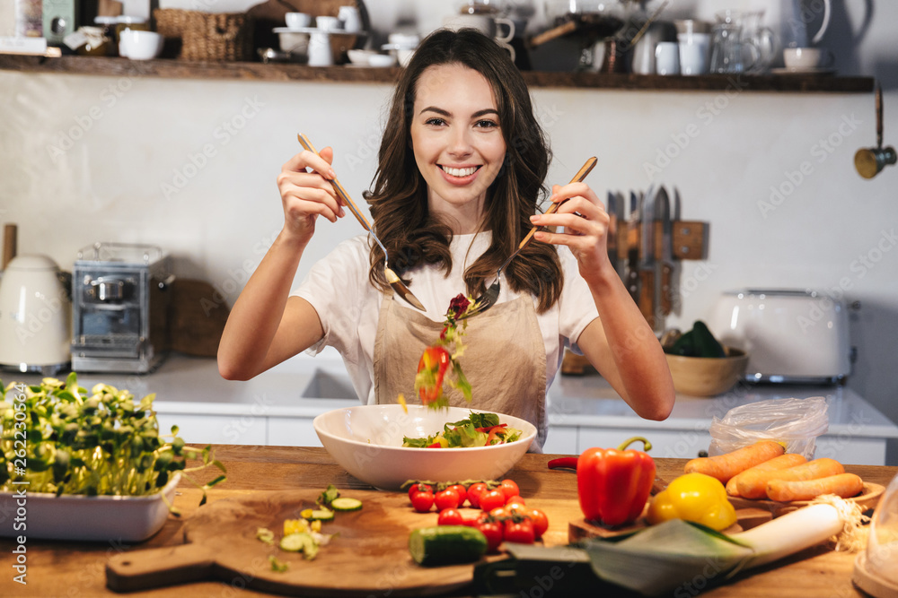 Beautiful young woman wearing apron cooking vegetables Beautiful young woman wearing apron cooking vegetables