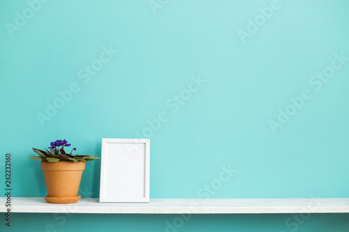 Modern room decoration with Picture frame mockup. White shelf against pastel turquoise wall with potted violet plant.