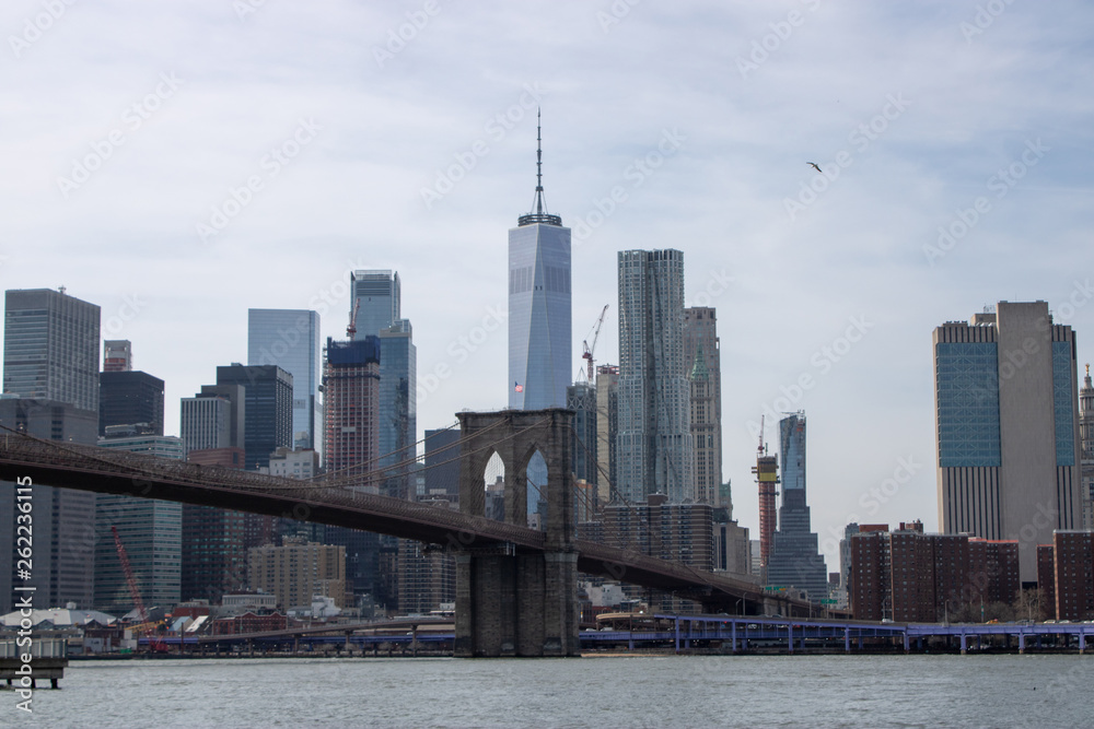 Fototapeta premium The famous Brooklyn Bridge Bridge located in New York City in the United States of America showing the suspension wired and the USA flag at the top of the column on a part cloudy day with blue Skys.