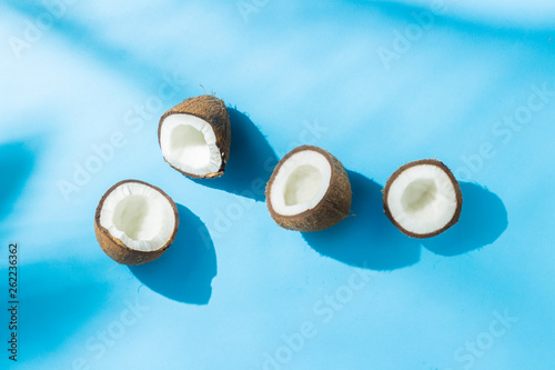 Broken coconut on a blue background under natural light with shadows. Hard light. Concept of diet, healthy eating, rest in the tropics, vacation and travel, vitamins. Flat lay, top view.