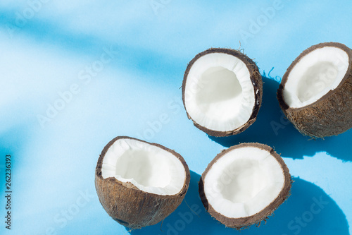 Broken coconut on a blue background under natural light with shadows. Hard light. Concept of diet, healthy eating, rest in the tropics, vacation and travel, vitamins.