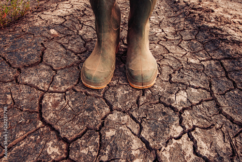 Farmer in rubber boots standing on dry soil ground