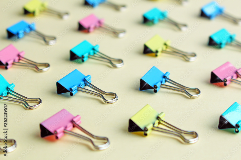 Top view of many multicolor binders clips on pastel beige background. Group of paper clip different colors. Top view of many multicolor binders clips on pastel beige background. Group of paper clip different colors.