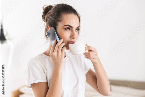 Student girl drinking coffee posing indoors talking by mobile phone.