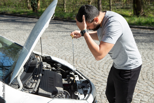 Stressed man with broken car looking at failed engine, trying to fix it