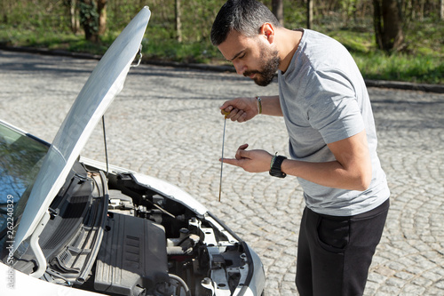Stressed man with broken car looking at failed engine, trying to fix it