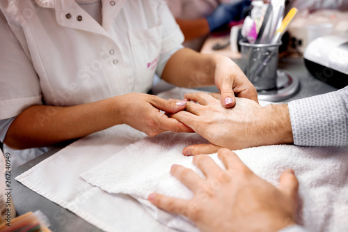 Manicurist making physical contact with her client by holding his hand during manicure grooming treatment