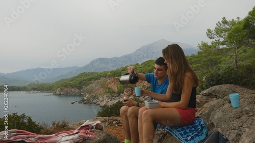 Young couple sitting on rocks in forest eating picnic