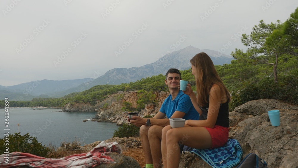 Young couple sitting on rocks in forest eating picnic