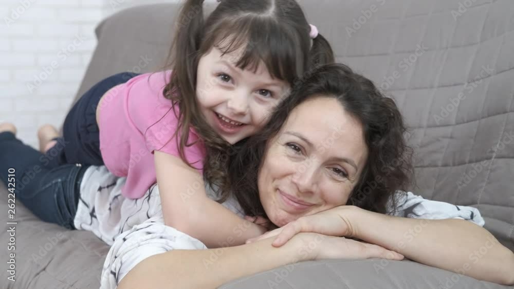 Happy child lying on mom. Charming little girl lies on her mother's back and hugs her. Happy child lying on mom. Charming little girl lies on her mother's back and hugs her.