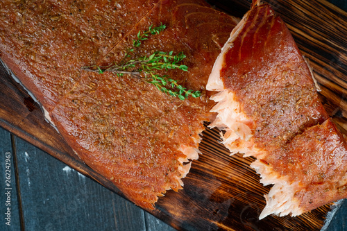 A half-torn piece of smoked salmon fillet on a wooden Board on a dark background