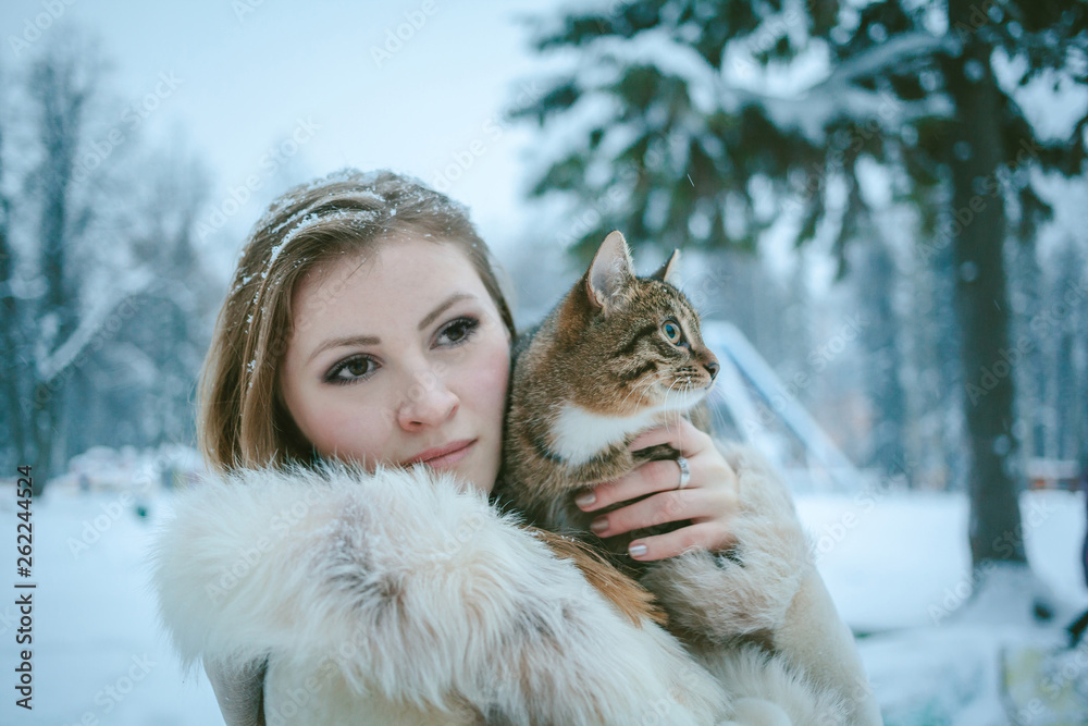 beautiful girl in a beige short fur coat with flowing hair holding a tabby color cat beautiful girl in a beige short fur coat with flowing hair holding a tabby color cat