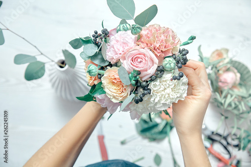 Top view cropped image of female florist arranging a bouquet with flowers use tools on white woodem background. Flowers delivery. Copy space. workplace and professional concept photo