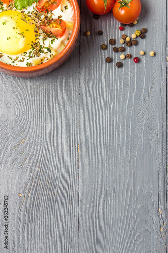 Portioned baked eggs in ceramic cocotte on gray wooden table, breakfast. Top view, copy space for you text.