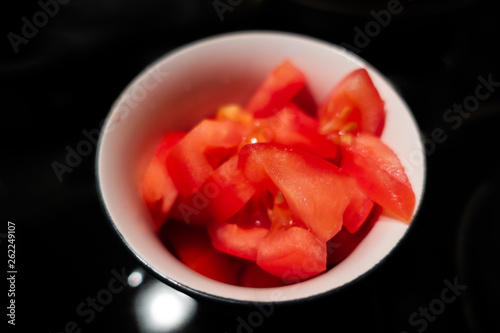 Diced tomatoes in white cup against black background. Selective focus.