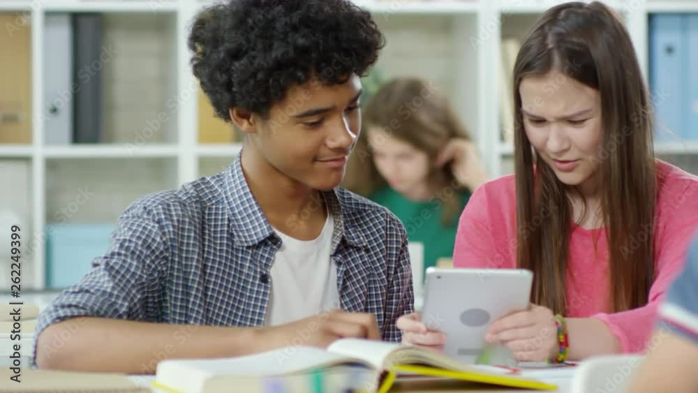Tracking right of mixed-race boy and Caucasian girl sitting at desk and using tablet Tracking right of mixed-race boy and Caucasian girl sitting at desk and using tablet