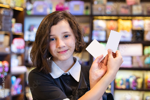 cute young teen girl holding white cards on the background of store shelves and smiling benevolently, close-up photo