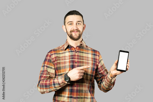 Young handsome man with facial hair posing over gray wall with a lot of copy space for text. Portrait of confident bearded male, wearing hipster slim fit checkered shirt. Isolated, background. © Evrymmnt