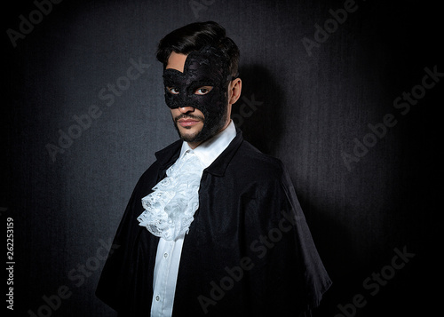 Young attractive man wearing a dark mask, dressed in a 10's-20's style with a white shirt and black cape