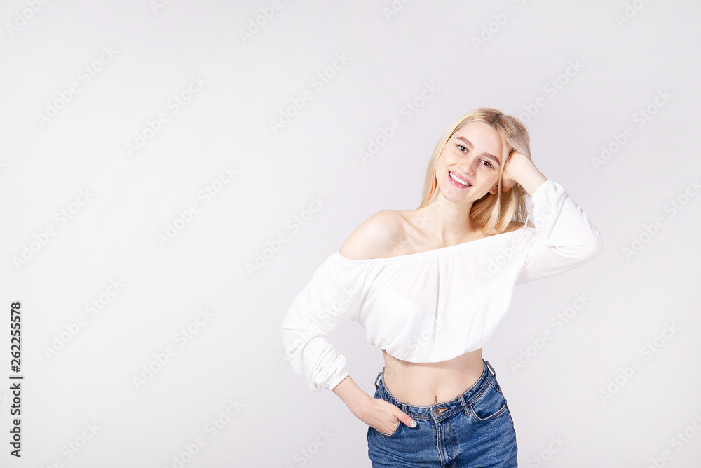 Studio shot of gorgeous young blonde woman with straight hair wearing off shoulder crop top sweater and high waisted denim shorts. Gray isolated background, copy space, close up.