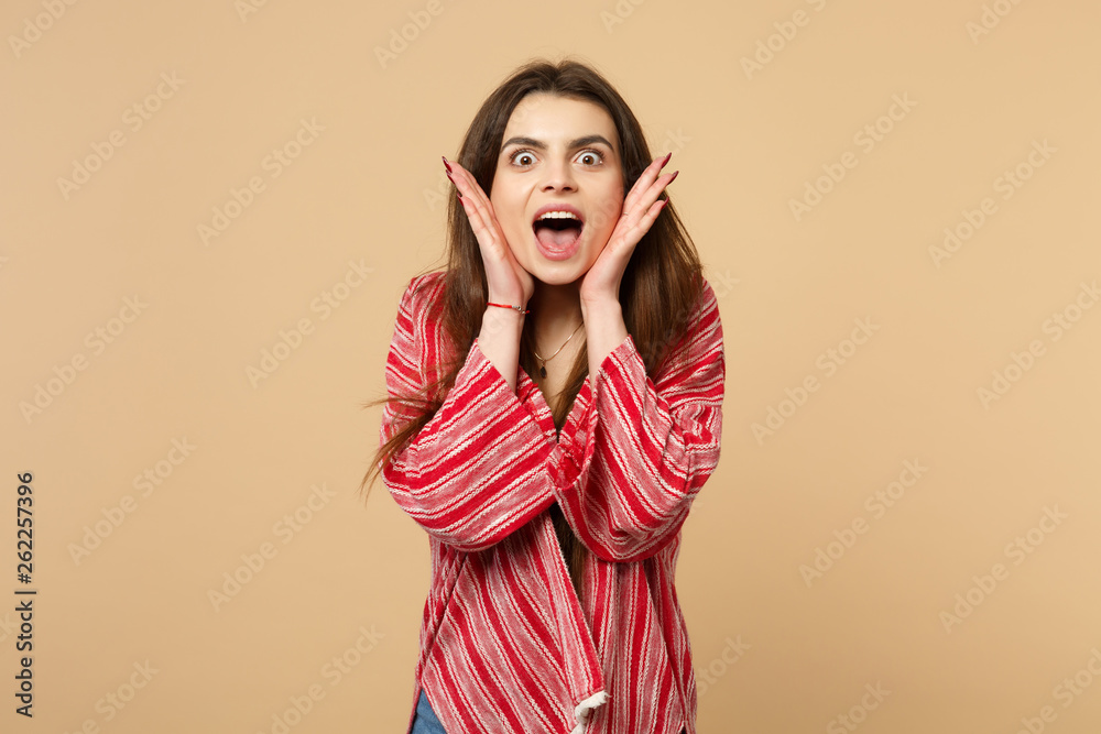 Portrait of amazed young woman in casual clothes keeping mouth wide open putting hands on face isolated on pastel beige wall background. People sincere emotions lifestyle concept. Mock up copy space.