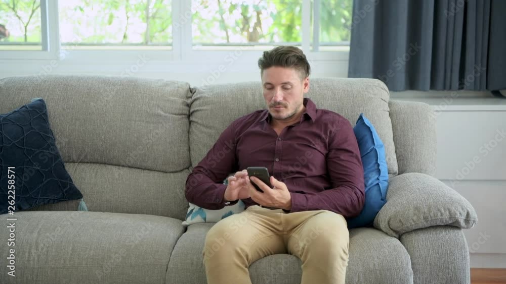Young man using phone on couch at home. Caucasian male, browsing internet. Focus mood. Young man using phone on couch at home. Caucasian male, browsing internet. Focus mood.