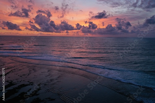 Aerial view of beautiful sunset in on the beach near Uluwatu Temple. Pink and orange sky  curly clouds and ocean.