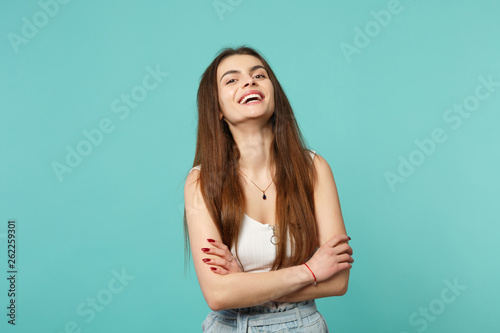 Portrait of laughing young woman in light casual clothes looking camera holding hands crossed isolated on blue turquoise wall background. People sincere emotions lifestyle concept. Mock up copy space. © ViDi Studio