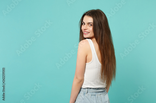 Back rear view of attractive cute young woman in light casual clothes looking back isolated on blue turquoise wall background in studio. People sincere emotions, lifestyle concept. Mock up copy space.