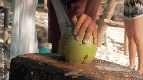 Close-up shot of man cuts off pieces from a young fresh coconut with a big knife for tasty content and juicy drink. Travel concept.