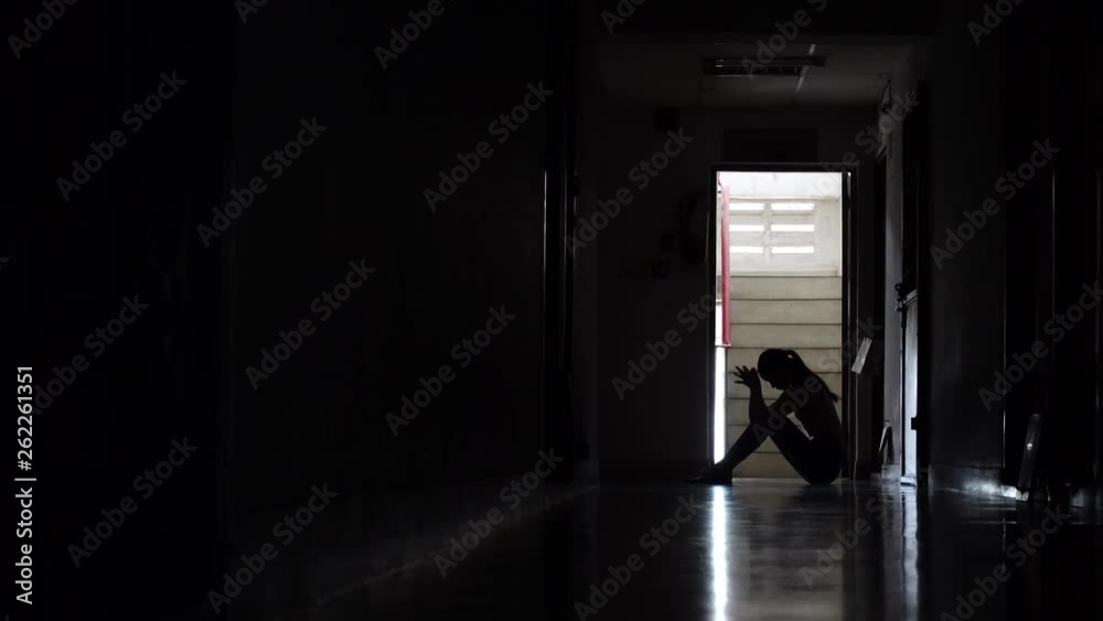 Silhouette of a sad young girl sitting in the dark leaning against the wall in old condo, Domestic violence, family problems, Stress, violence, The concept of depression and suicide. Silhouette of a sad young girl sitting in the dark leaning against the wall in old condo, Domestic violence, family problems, Stress, violence, The concept of depression and suicide.