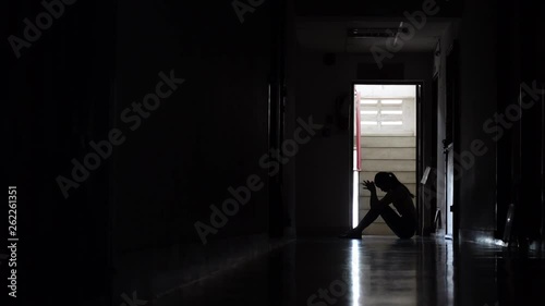 Silhouette of a sad young girl sitting in the dark leaning against the wall in old condo, Domestic violence, family problems, Stress, violence, The concept of depression and suicide.