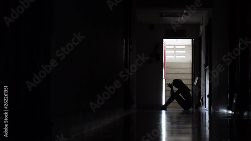 Silhouette of a sad young girl sitting in the dark leaning against the wall in old condo, Domestic violence, family problems, Stress, violence, The concept of depression and suicide. photo
