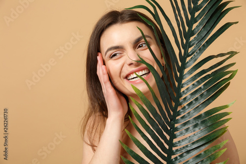 Close up brunette half naked woman 20s with perfect skin, nude make up palm leaf isolated on beige pastel wall background, studio portrait. Health care cosmetic procedures concept. Mock up copy space.