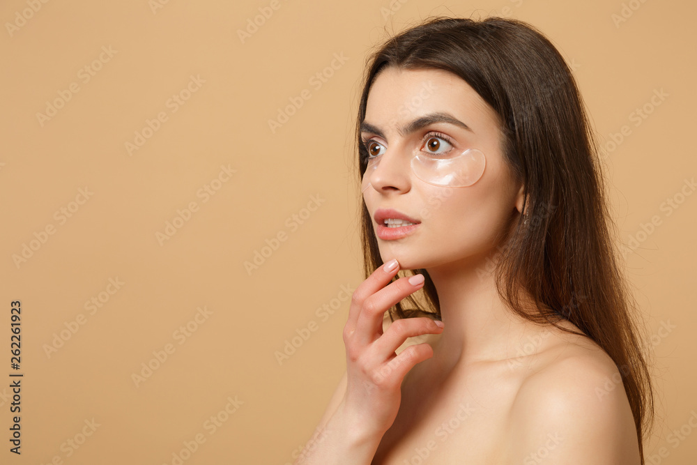 Close up half naked woman 20s with perfect skin, nude make up patches under eyes isolated on beige pastel wall background, studio portrait. Health care cosmetic procedures concept. Mock up copy space. Close up half naked woman 20s with perfect skin, nude make up patches under eyes isolated on beige pastel wall background, studio portrait. Health care cosmetic procedures concept. Mock up copy space.