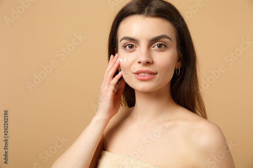 Close up half naked woman 20s with perfect skin nude make up applying facial cream isolated on beige pastel wall background, studio portrait. Healthcare cosmetic procedures concept. Mock up copy space