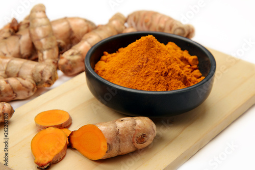 Organic healthy Turmeric powder in a bowl with Turmeric roots on white background