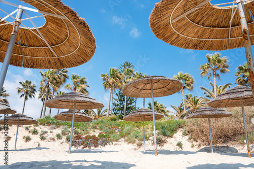 Reed beach umbrellas  sunshades against blue sky on the beach. Bamboo parasols  straw umbrellas on on white sandy tropical seashore. Tropical sea beach coastline  summer holiday.