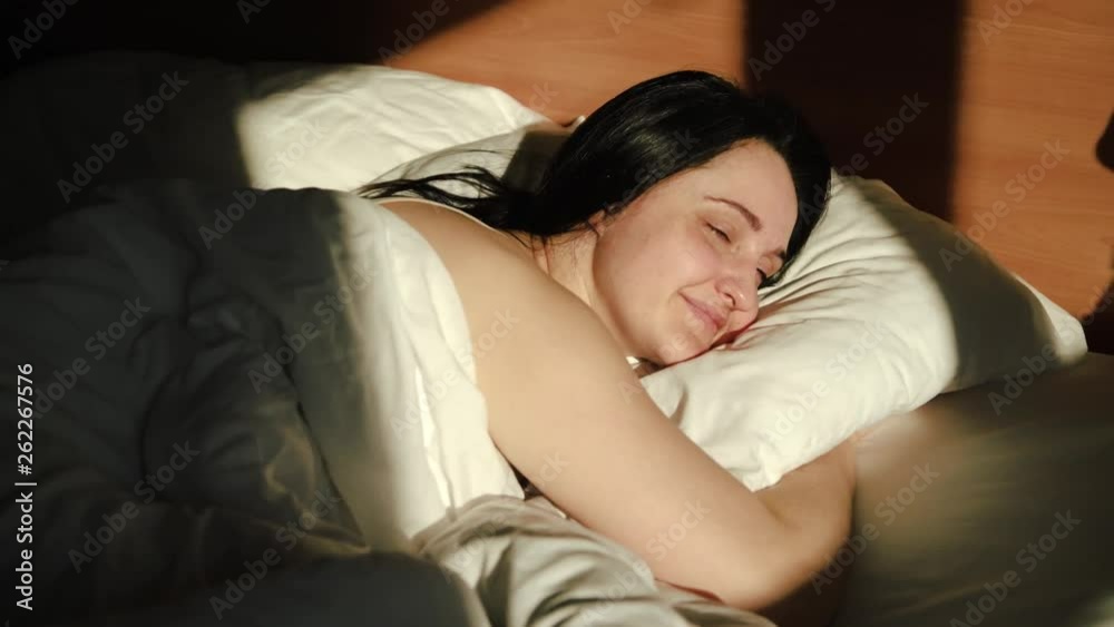 A young, beautiful girl wakes up in the morning and enjoys the first rays of the sun. Hugs the pillow A young, beautiful girl wakes up in the morning and enjoys the first rays of the sun. Hugs the pillow