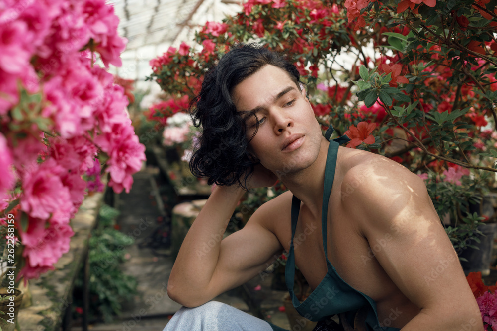 Attractive muscular florist with naked torso sitting among colorful flowers Attractive muscular florist with naked torso sitting among colorful flowers