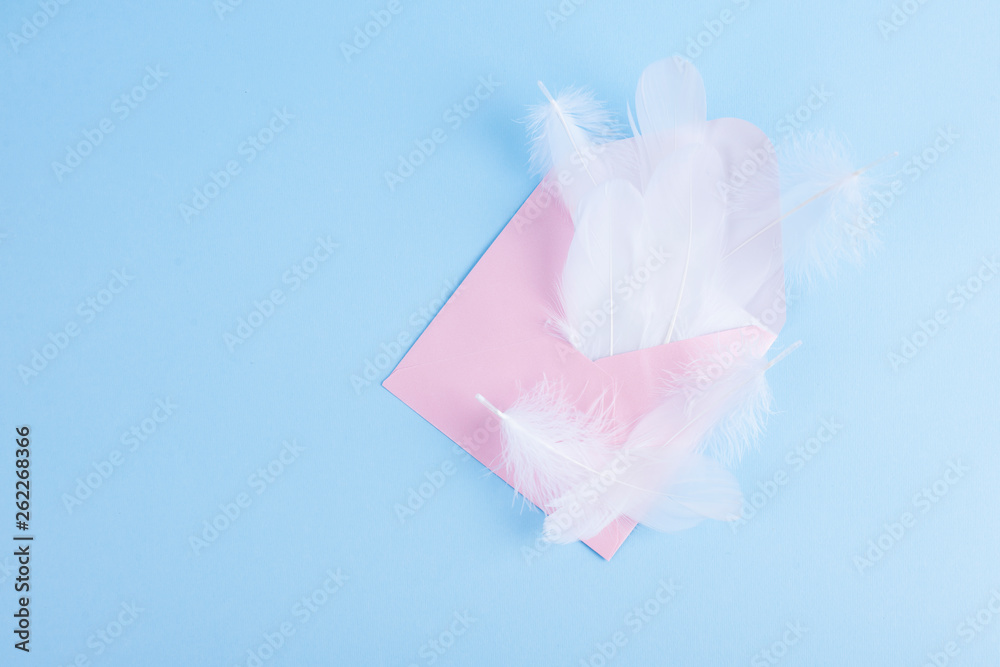 Fototapeta premium Piume bianche e busta rosa per lettere su sfondo blu. Copy space.