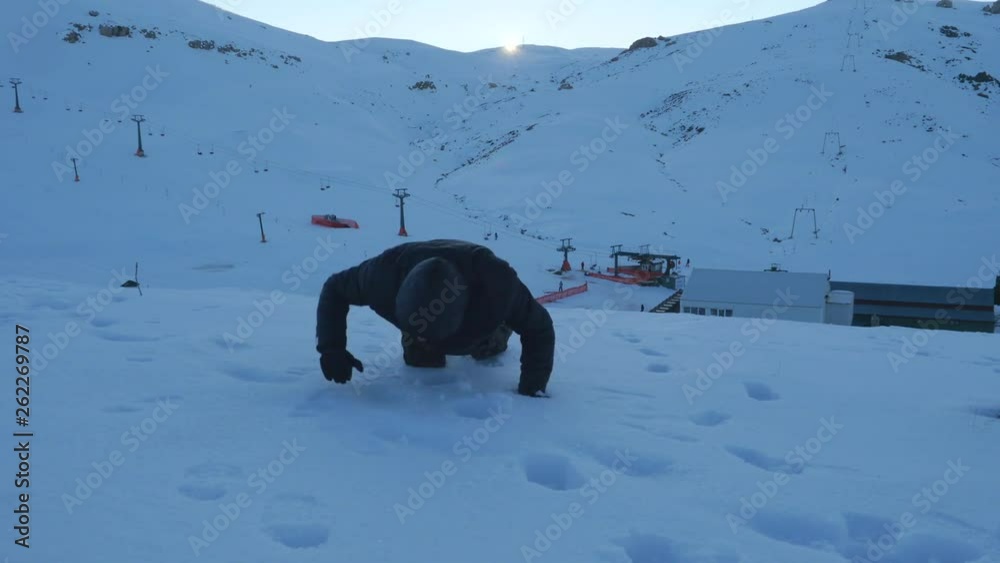 Young man in dark clothes falling down exhausted on a snowy mountain